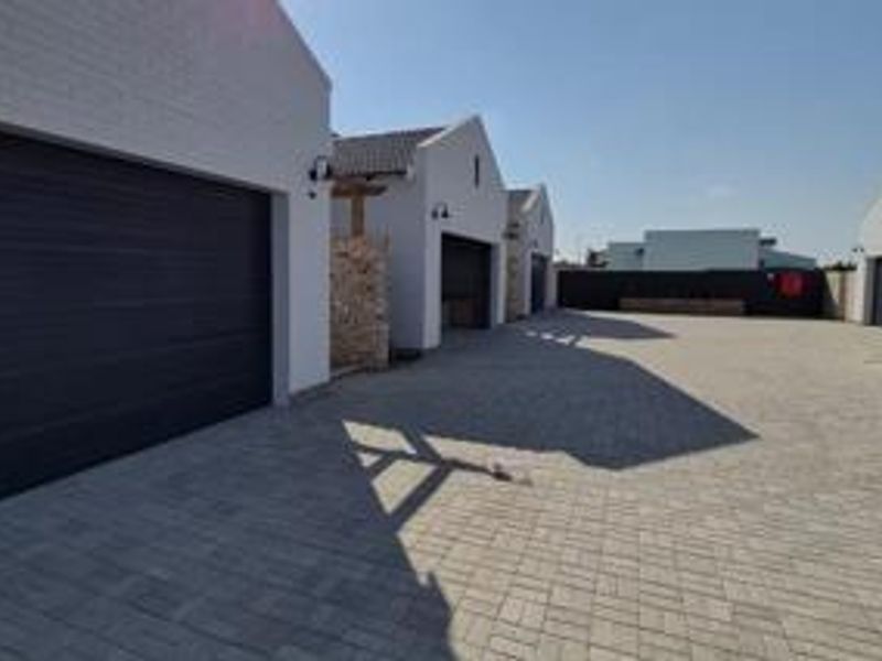 A well-maintained paved driveway area featuring multiple garage entrances and modern stone cladding accents on the townhouse exterior.