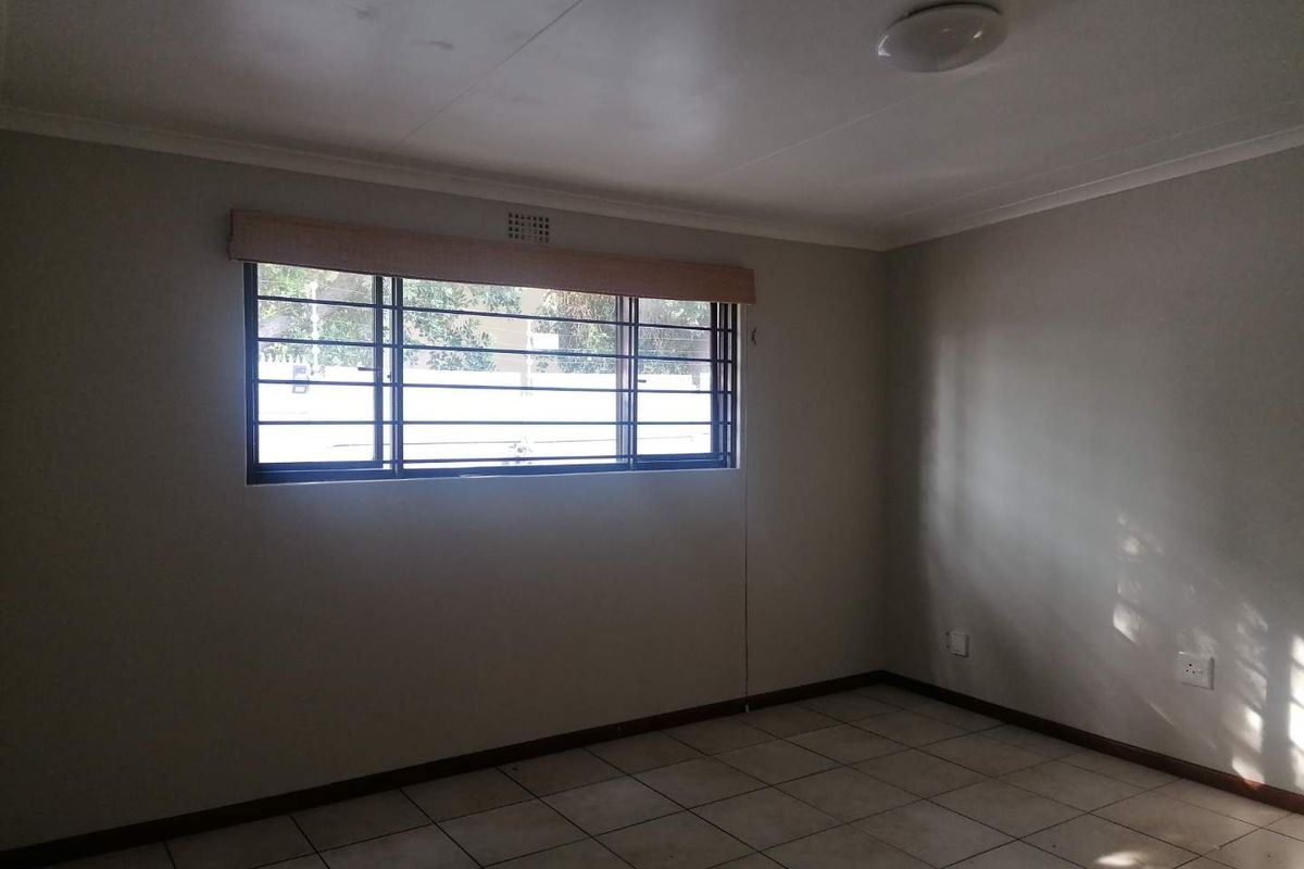 A clean, empty bedroom featuring neutral tiled flooring, security bars on the window, and a simple ceiling light fixture.
