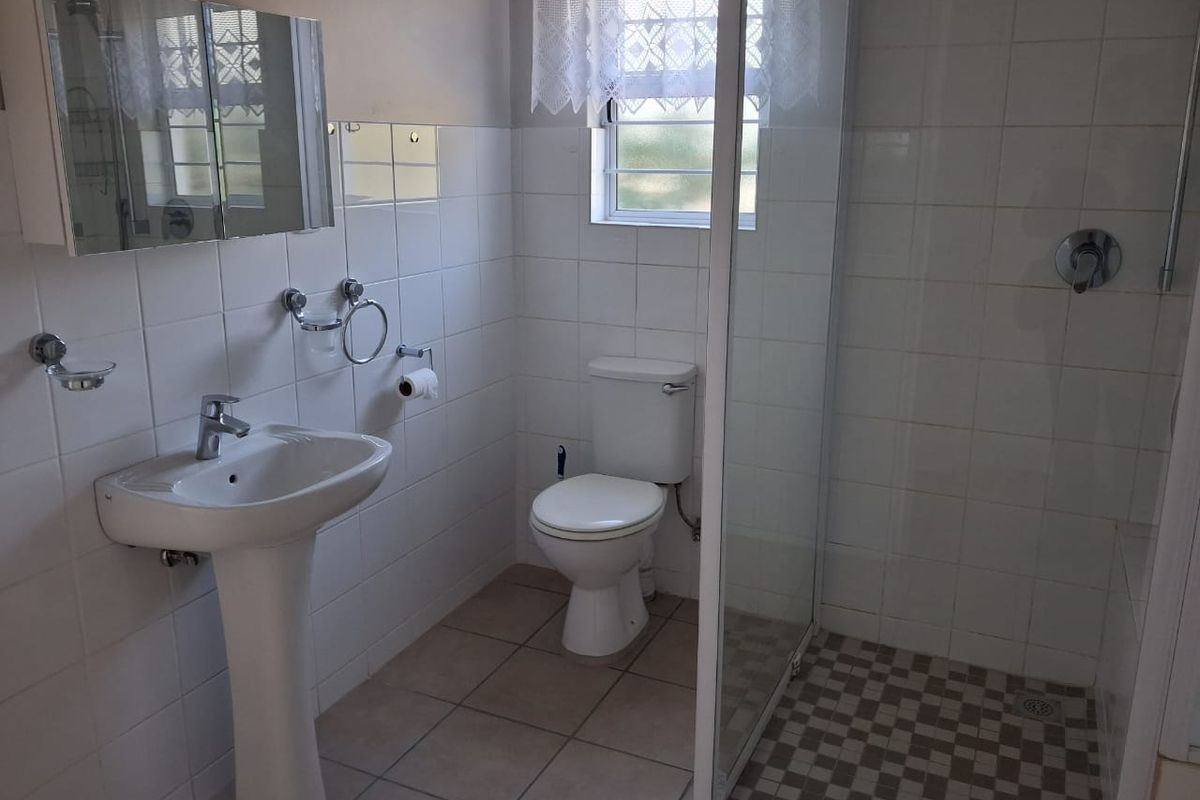 A functional bathroom featuring a pedestal basin, a glass-enclosed shower, and a toilet, finished with neutral wall and floor tiles.