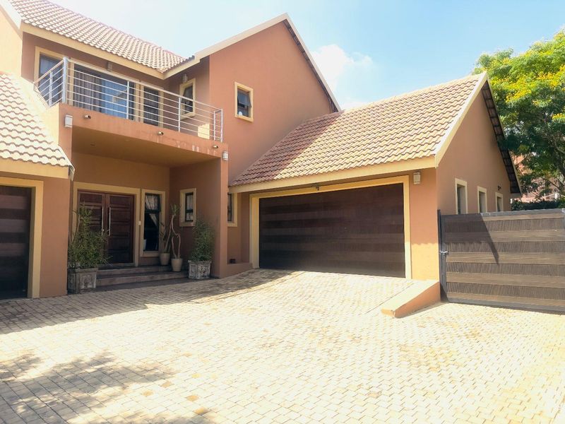 Front elevation of a double-story house featuring a paved driveway, integrated double garage, and an upper-level balcony with stainless steel railings.