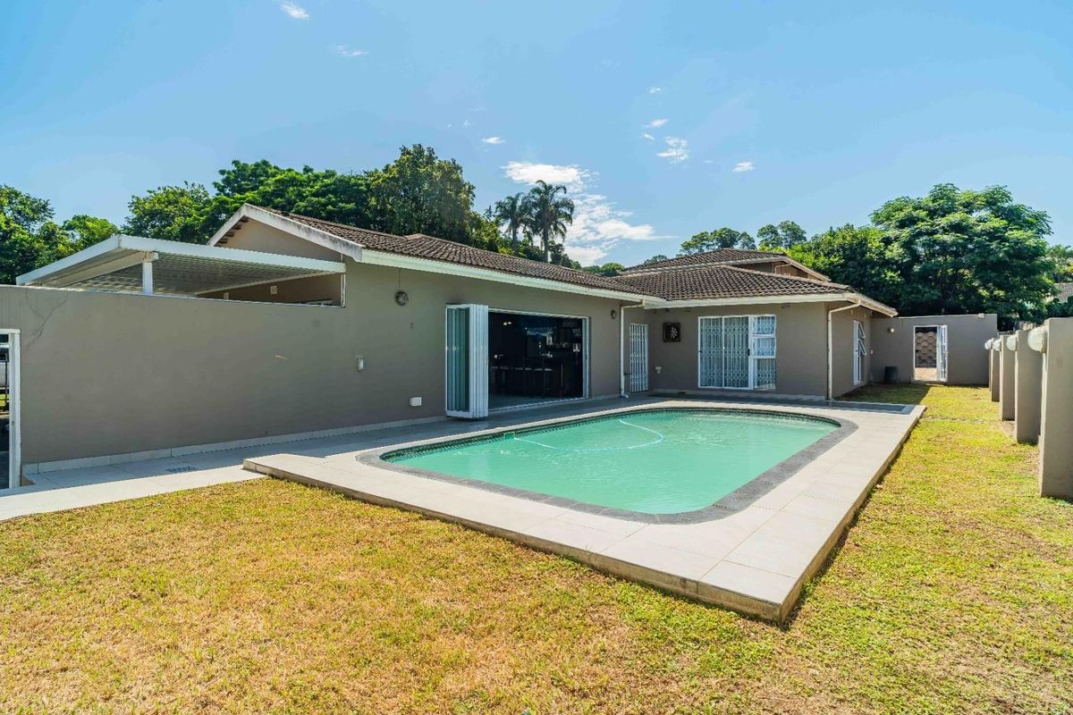 Rear exterior view of the property featuring a swimming pool with tiled surround, covered patio area, and bi-fold doors leading into the home.