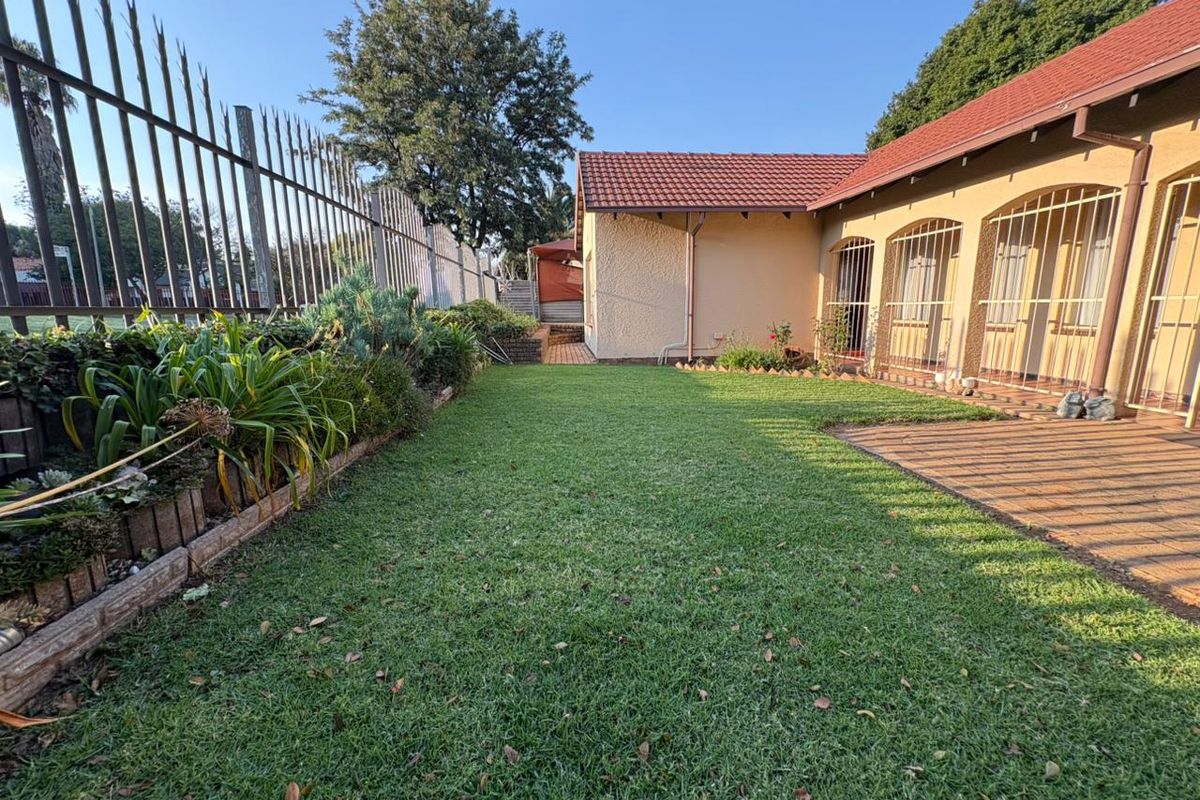 A well-maintained rear garden featuring a manicured lawn, paved patio area, and secure perimeter fencing along the property boundary.