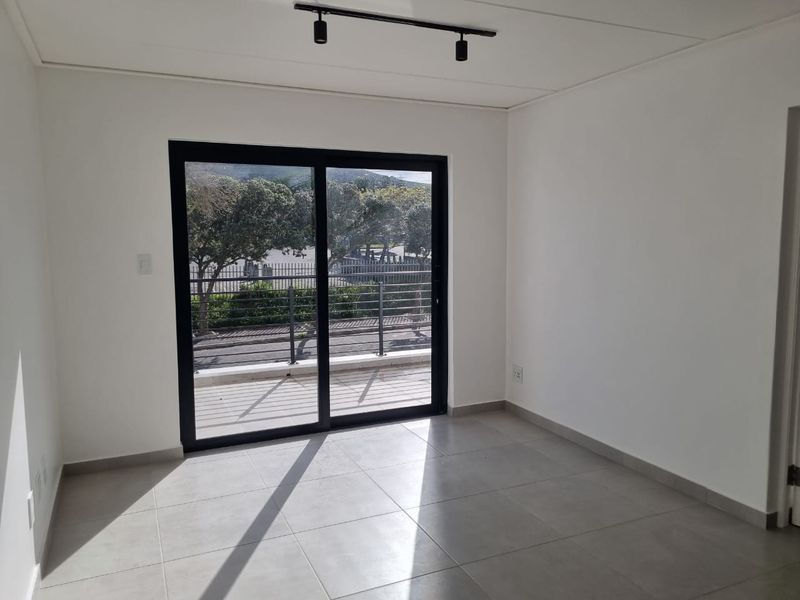A bright, empty living area featuring modern tiled flooring, track lighting, and a large sliding glass door providing access to an outdoor balcony.
