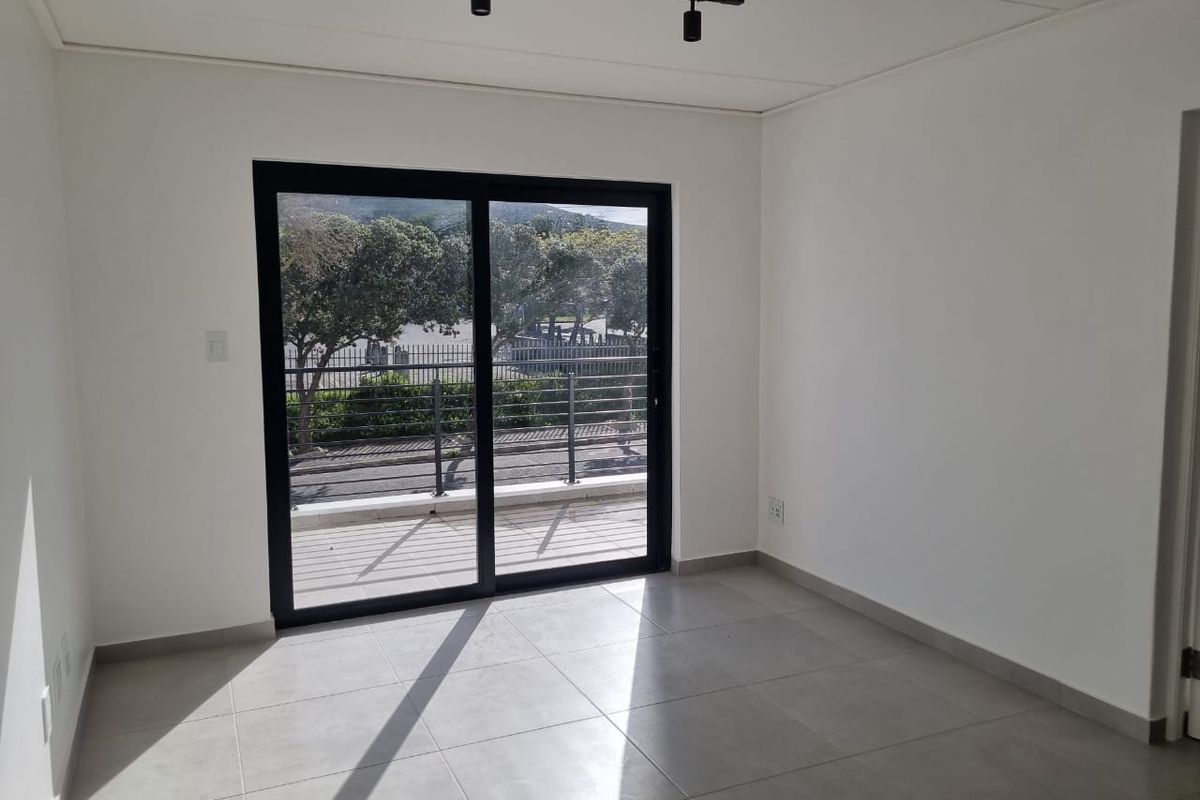 A bright, empty living area featuring modern tiled flooring, track lighting, and a large sliding glass door providing access to an outdoor balcony.