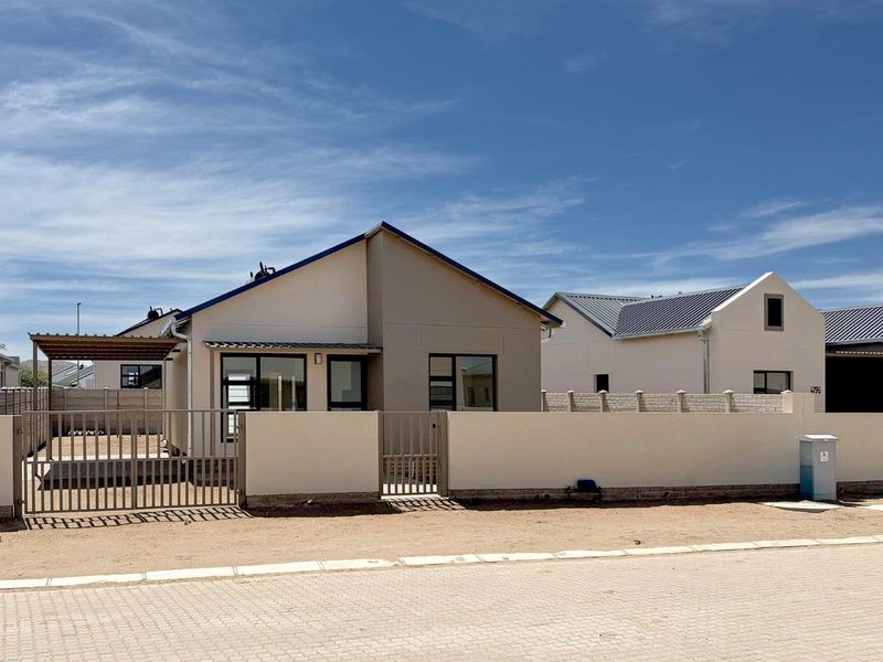 Front view of a modern single-story house featuring a metal roof, perimeter wall with gate, and a paved driveway area.