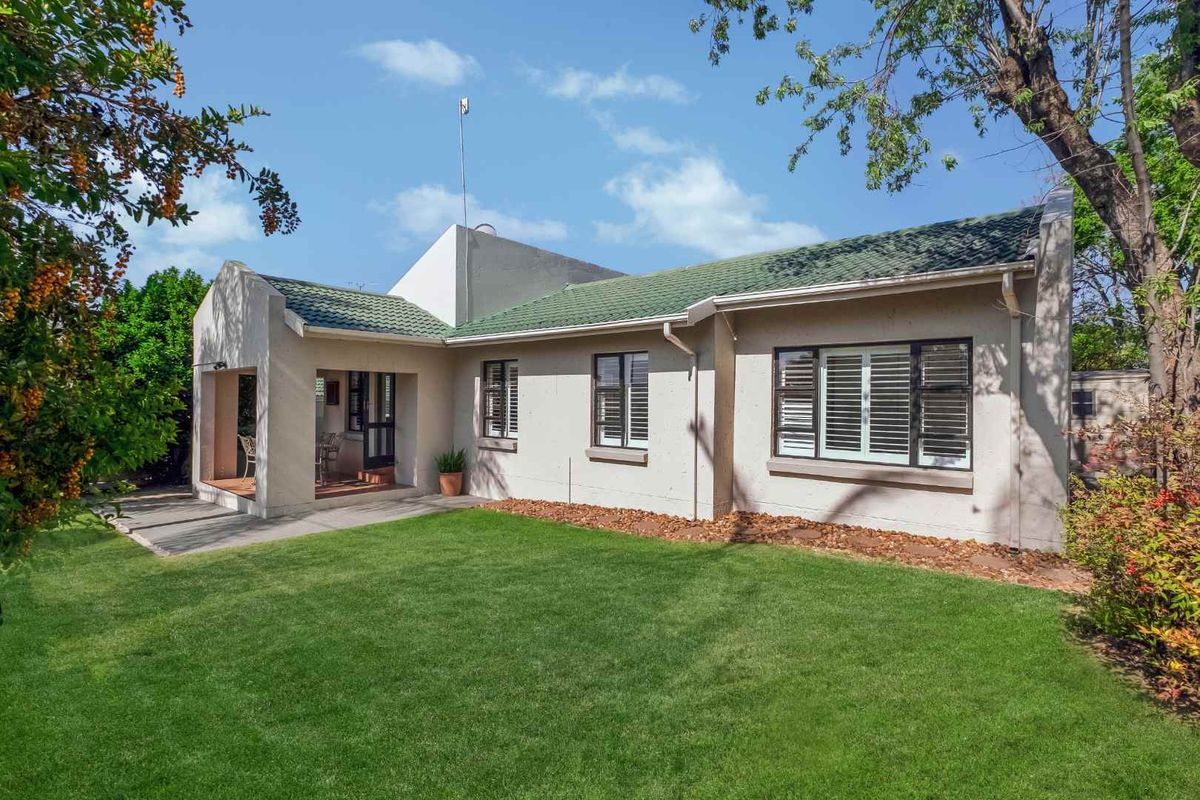 Rear view of the house featuring a well-maintained lawn, a covered patio area, and classic window shutters.