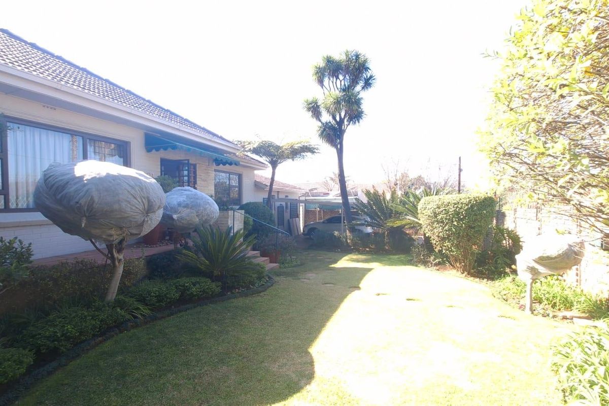 A well-maintained rear garden featuring a lawn, established landscaping, and a covered patio area attached to the main house structure.