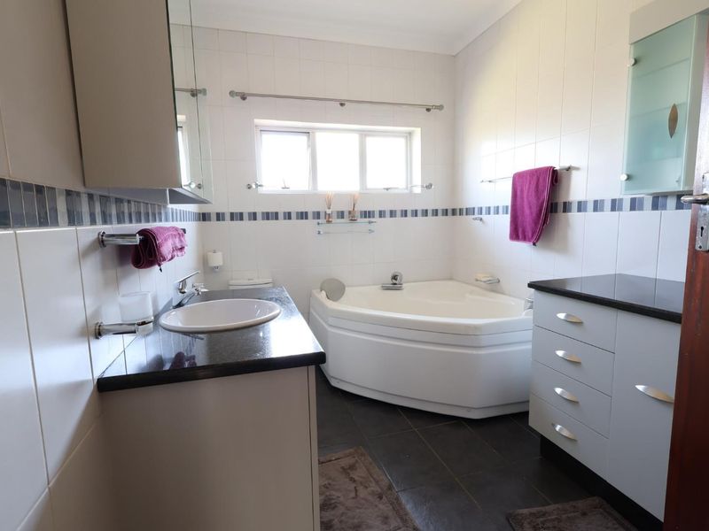 A functional bathroom featuring a corner bathtub, vanity with granite countertop, and tiled finishes throughout.
