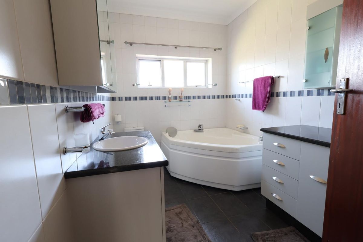 A functional bathroom featuring a corner bathtub, vanity with granite countertop, and tiled finishes throughout.