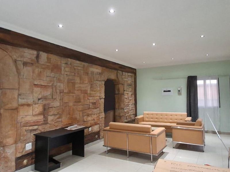 Open plan living area featuring a prominent stone accent wall, recessed downlighting, and neutral tiled flooring, providing a spacious and versatile layout.