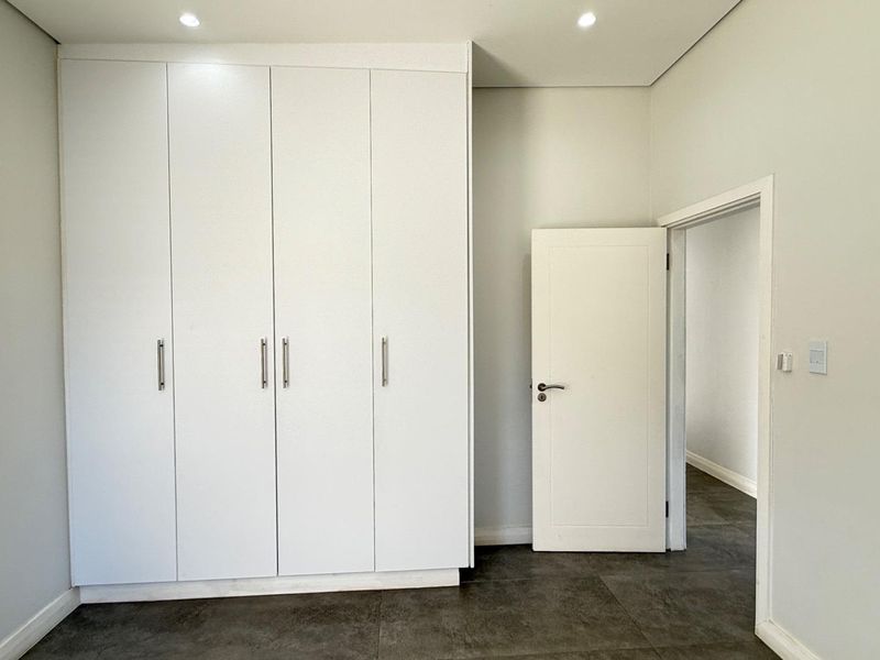 A clean, modern bedroom featuring neutral walls, dark tiled flooring, and ample built-in cupboard storage with recessed lighting.
