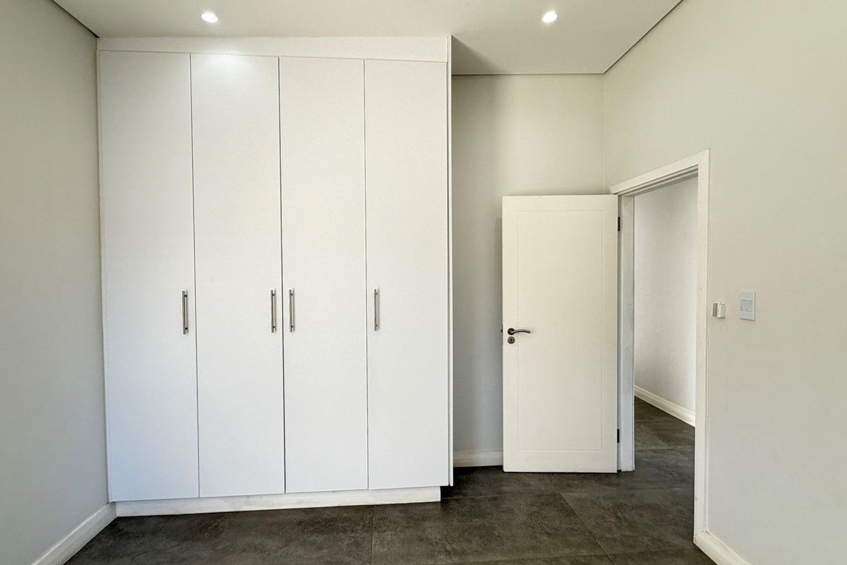 A clean, modern bedroom featuring neutral walls, dark tiled flooring, and ample built-in cupboard storage with recessed lighting.