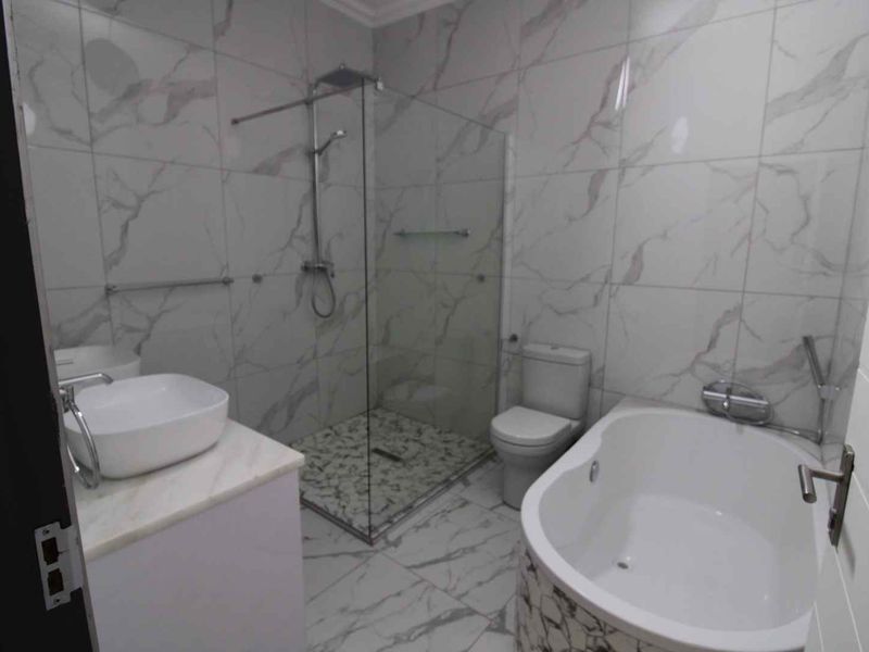 Modern bathroom featuring a walk-in shower with glass screen, a freestanding bathtub, and a vessel sink vanity with marble-look tiling throughout.