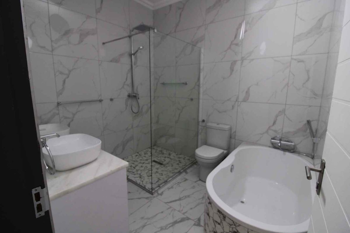 Modern bathroom featuring a walk-in shower with glass screen, a freestanding bathtub, and a vessel sink vanity with marble-look tiling throughout.