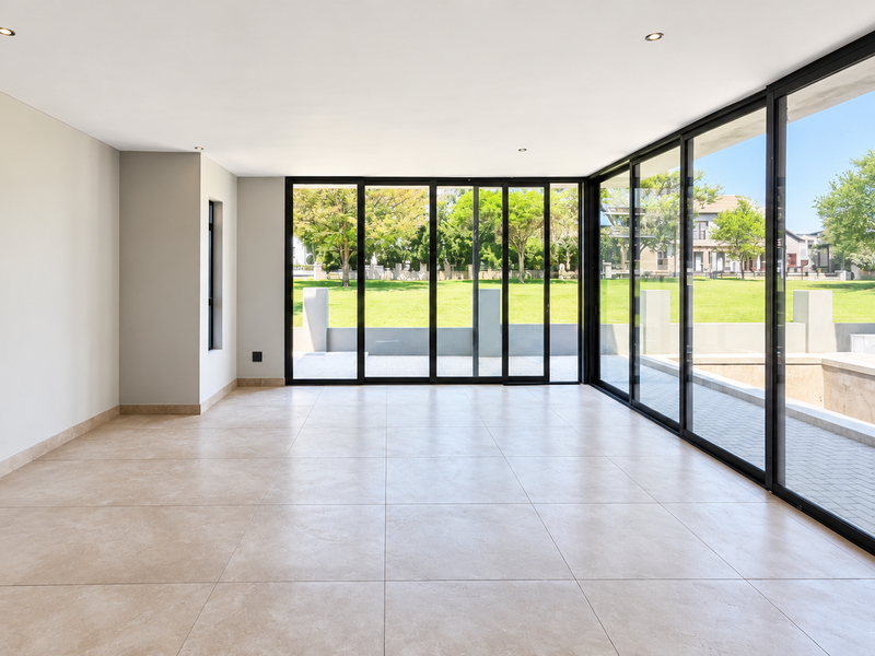 Spacious, light-filled living area featuring large format floor tiles and expansive black aluminium sliding doors that open onto a private garden view.