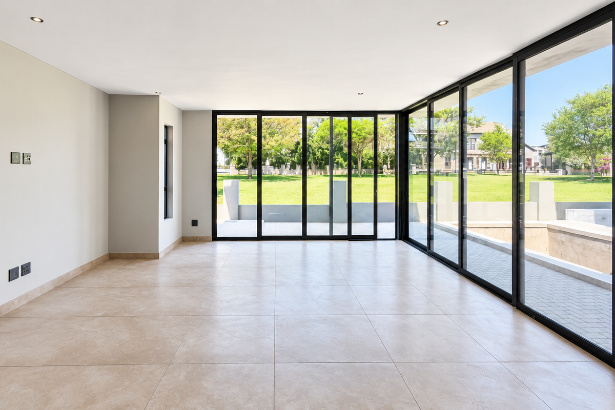 Spacious, light-filled living area featuring large format floor tiles and expansive black aluminium sliding doors that open onto a private garden view.