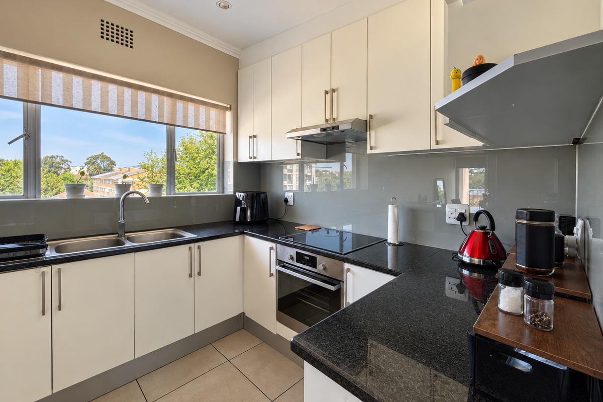 Modern kitchen featuring sleek white cabinetry, dark granite countertops, integrated stainless steel appliances, and a glass splashback with ample natural light.