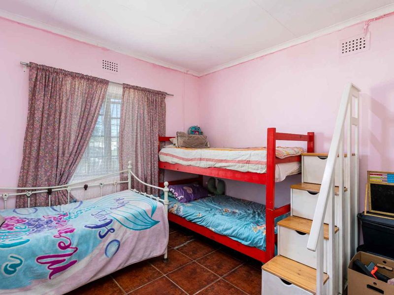 A bedroom featuring tiled flooring and ventilation grilles, currently utilized as a children's room with pink wall finishes.