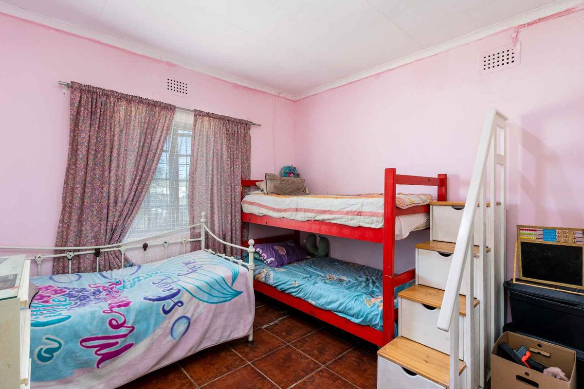 A bedroom featuring tiled flooring and ventilation grilles, currently utilized as a children's room with pink wall finishes.