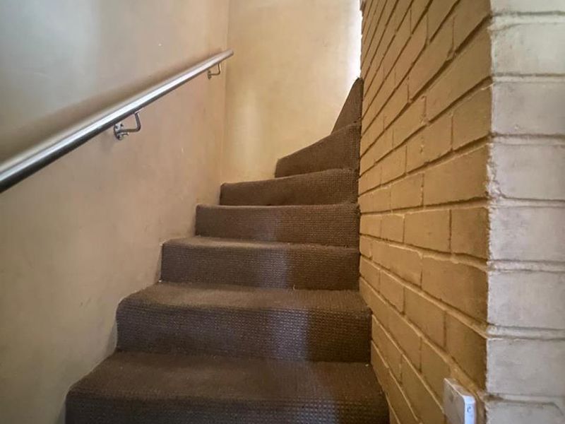 A staircase featuring carpeted steps, a metal handrail, and an exposed brick feature wall.