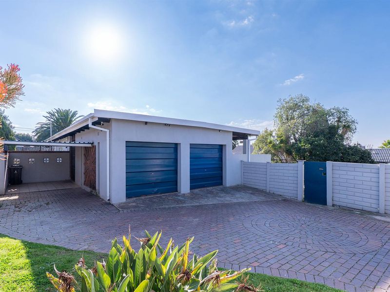A detached double garage with a paved driveway, carport, and secure boundary walling in a residential setting.