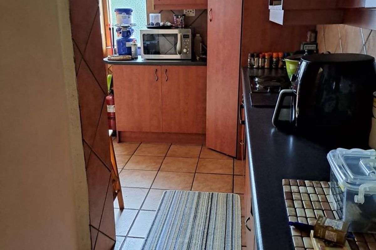 A functional galley-style kitchen featuring wood-tone cabinetry, dark countertops, and tiled flooring, providing a practical layout for daily meal preparation.
