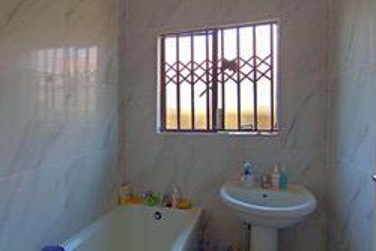 A functional bathroom featuring marble-look wall tiles, a pedestal basin, and a bathtub, secured with metal burglar bars on the window.
