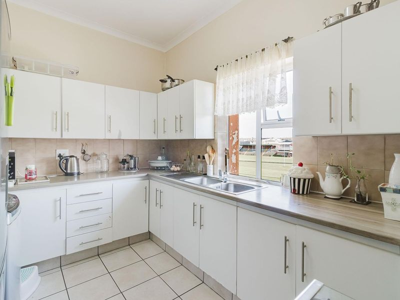 A functional kitchen featuring white cabinetry, laminate countertops, a stainless steel double sink, and tiled flooring with a view of the exterior.