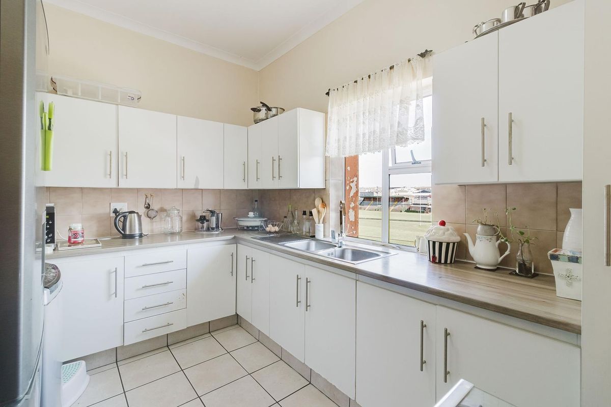 A functional kitchen featuring white cabinetry, laminate countertops, a stainless steel double sink, and tiled flooring with a view of the exterior.