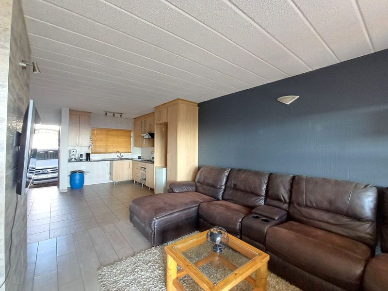 Open-plan living area featuring a functional kitchen with built-in cabinetry, integrated appliances, and tiled flooring, seamlessly connecting to the lounge space.