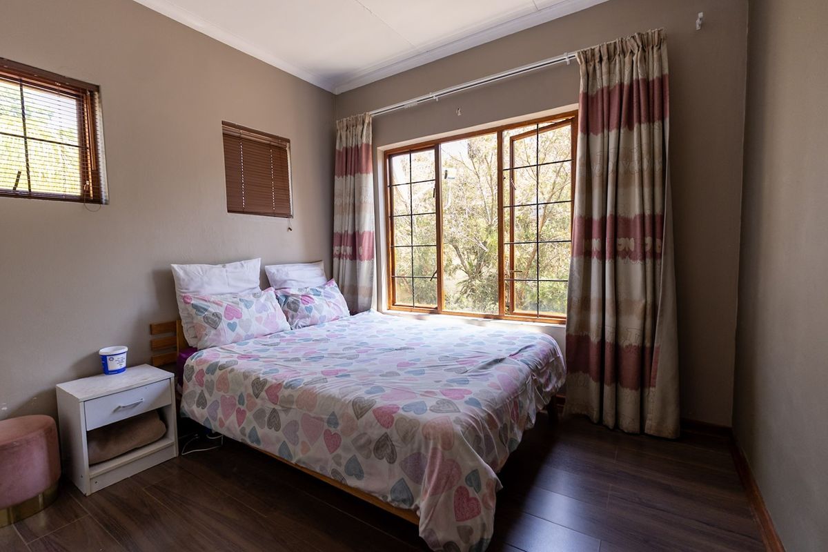 A bedroom featuring laminate flooring, wooden window frames, and neutral wall tones, offering a functional space with natural light.