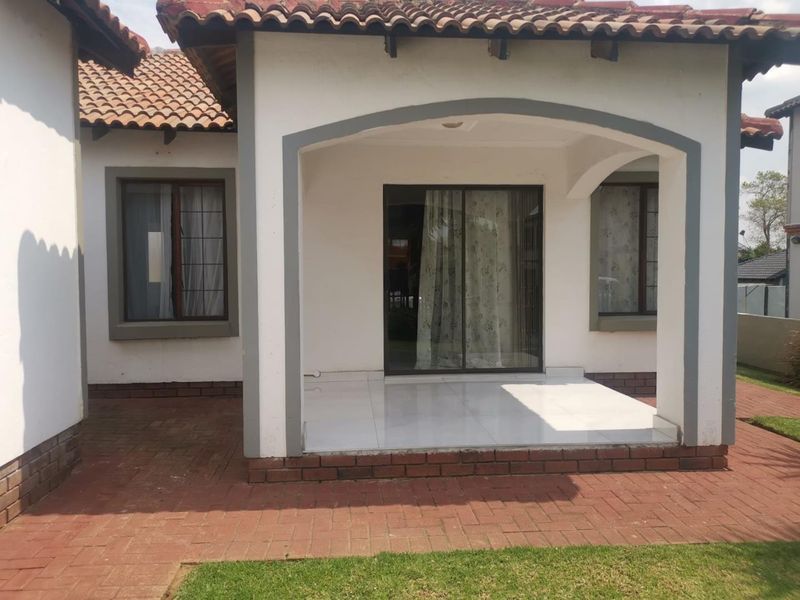 A covered patio area featuring tiled flooring, brick paving, and an arched entrance leading into the home through a sliding glass door.