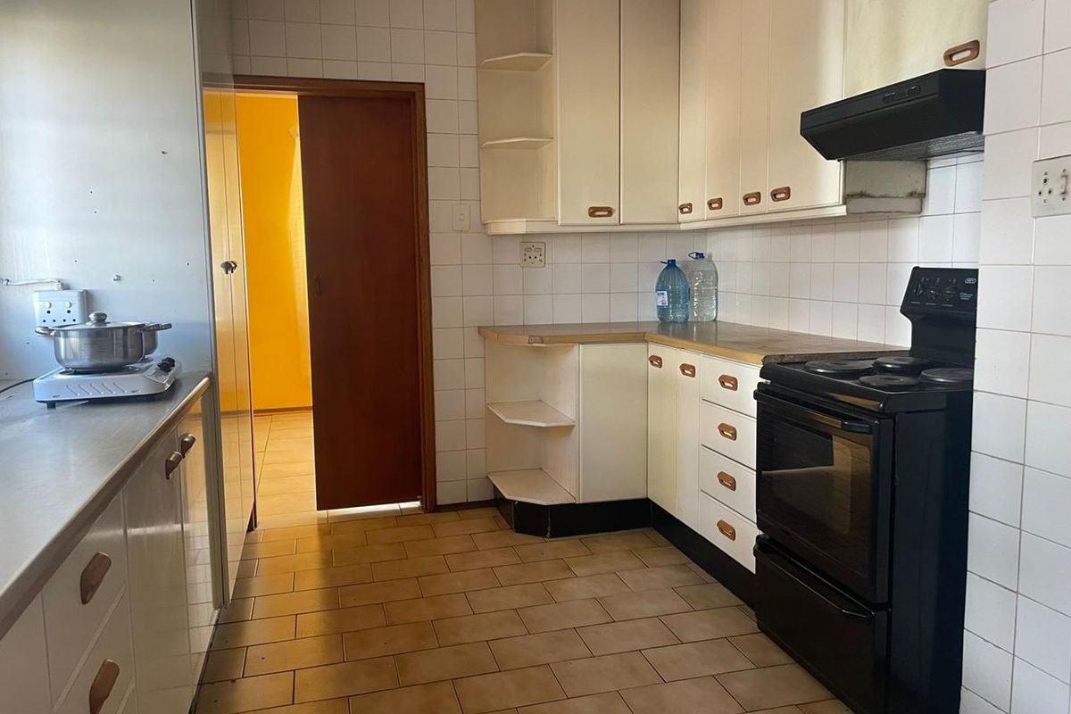 A functional kitchen featuring dated cabinetry, tiled splashbacks, and tiled flooring, offering significant potential for a modern renovation.