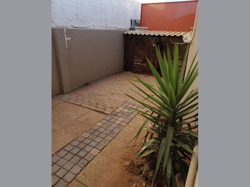 A small, paved rear courtyard area featuring a boundary wall and a small storage structure, offering potential for outdoor improvement.