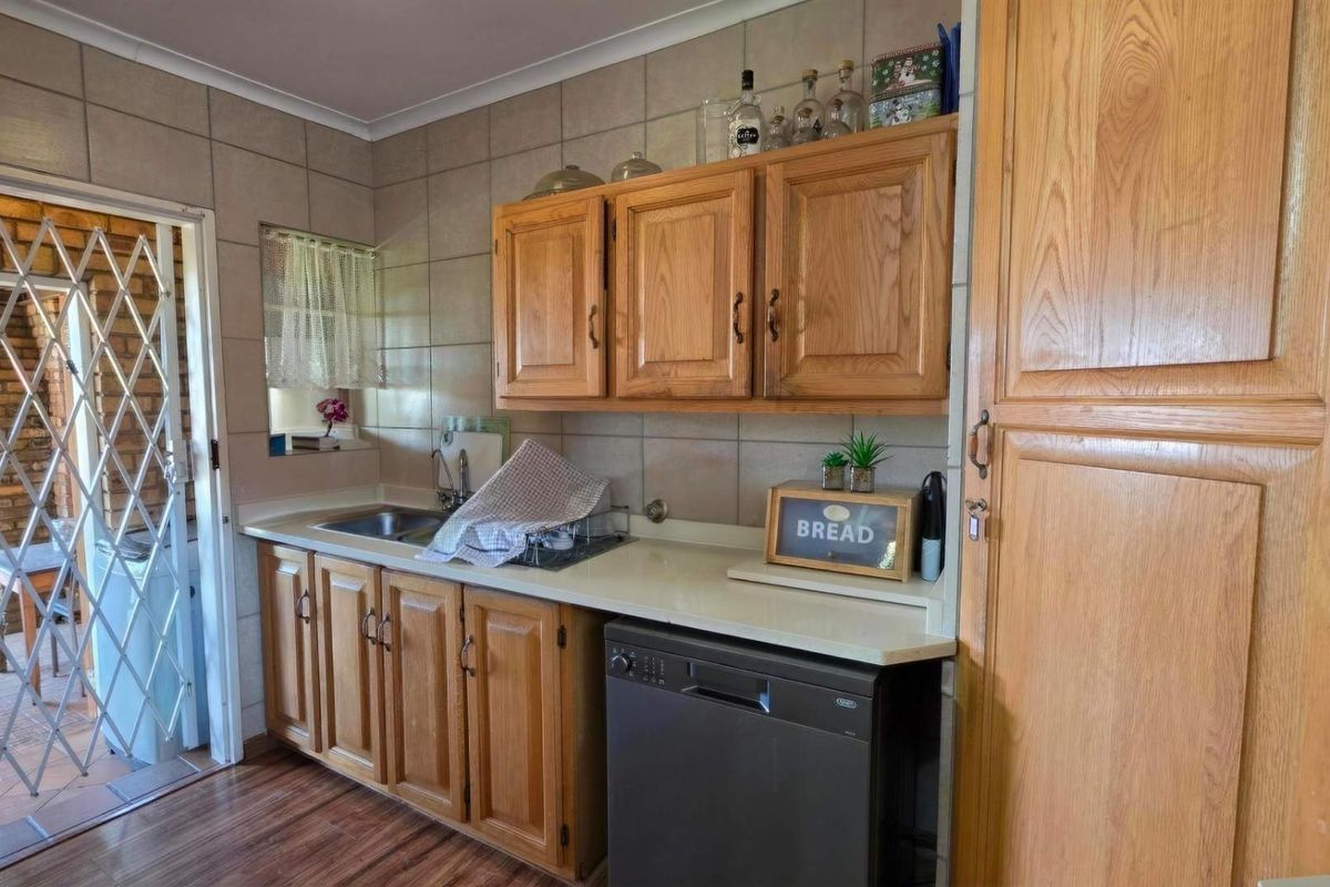 A functional kitchen featuring wooden cabinetry, tiled backsplash, and laminate countertops, with direct access to an outdoor area through a security gate.