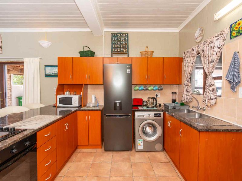 A functional kitchen featuring wooden cabinetry, laminate countertops, a double basin sink, and integrated appliances with tiled flooring and a timber ceiling.