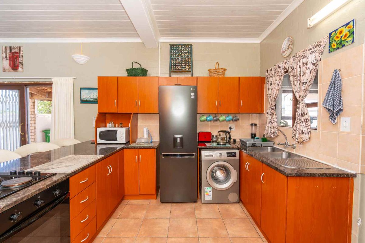 A functional kitchen featuring wooden cabinetry, laminate countertops, a double basin sink, and integrated appliances with tiled flooring and a timber ceiling.