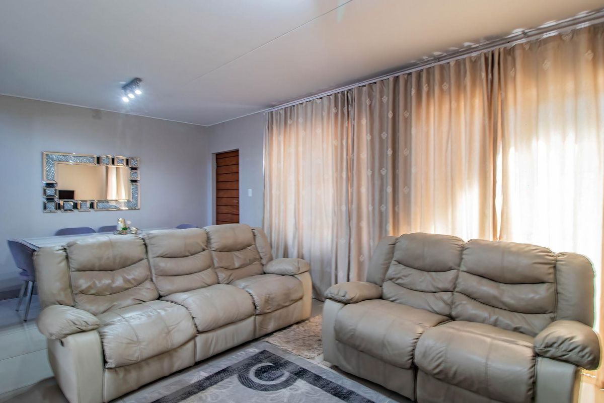 A well-maintained living room featuring tiled flooring, recessed lighting, and large windows with full-length curtains, providing a bright and comfortable living space.