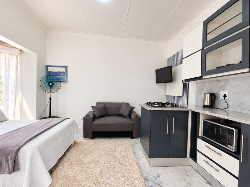 A modern open-plan studio apartment featuring a compact kitchenette with built-in cabinetry, gas hob, and marble-effect flooring throughout.