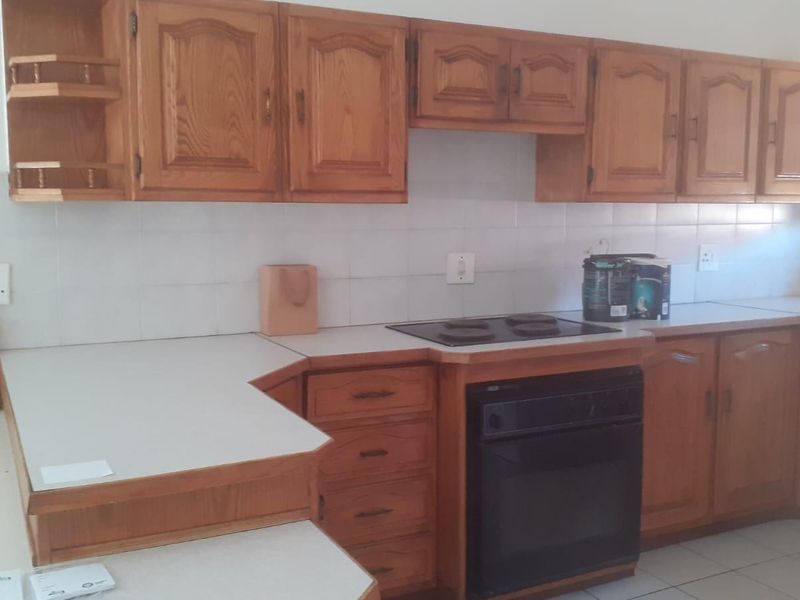 A functional kitchen featuring traditional wooden cabinetry, laminate countertops, a built-in oven, and an electric hob with a tiled backsplash.