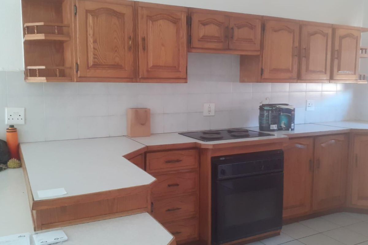 A functional kitchen featuring traditional wooden cabinetry, laminate countertops, a built-in oven, and an electric hob with a tiled backsplash.