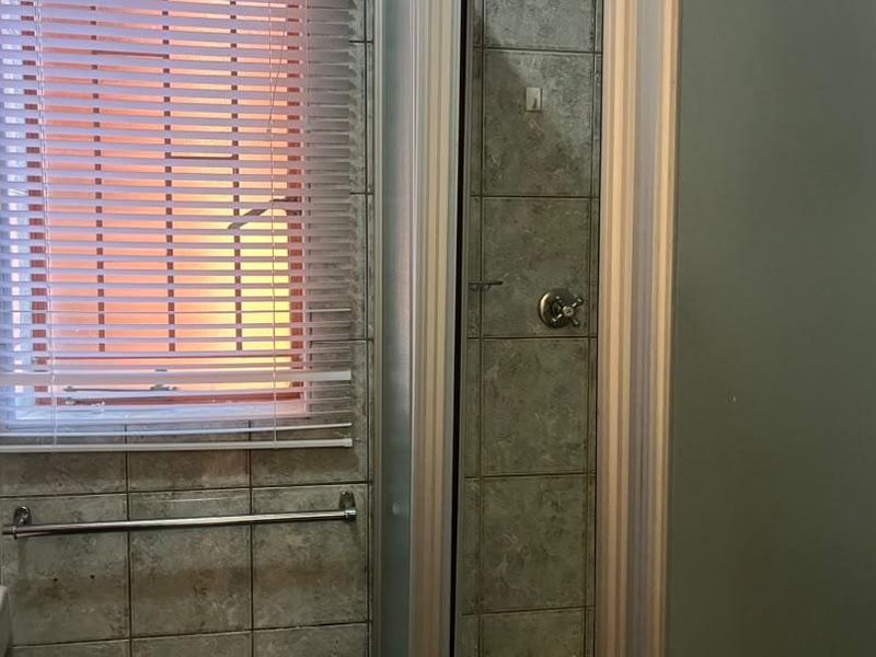 A functional bathroom featuring tiled walls, a shower enclosure, and a basin, presenting a dated aesthetic suitable for modernization.