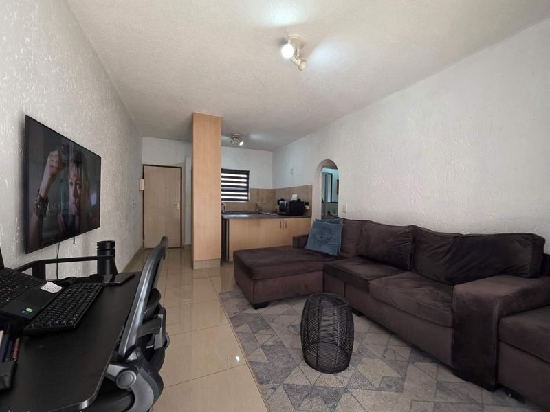 Open-plan living area featuring tiled flooring, textured walls, and a compact kitchen space with built-in cabinetry.