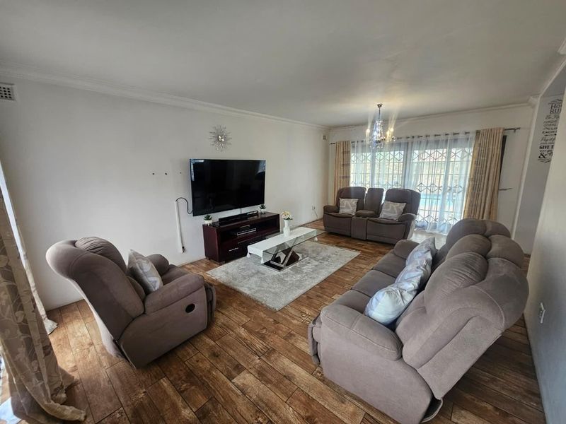 A spacious living room featuring laminate wood flooring, coved cornicing, and a large sliding glass door with security gate providing access to the exterior.