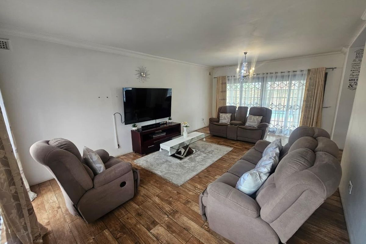 A spacious living room featuring laminate wood flooring, coved cornicing, and a large sliding glass door with security gate providing access to the exterior.
