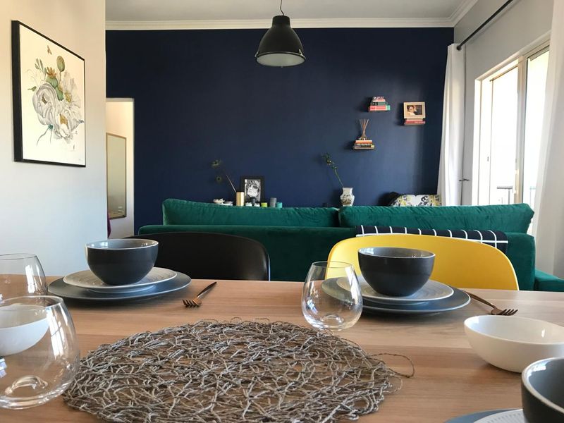 An open-plan living and dining area featuring a bold navy accent wall, modern pendant lighting, and access to an outdoor space via sliding doors.