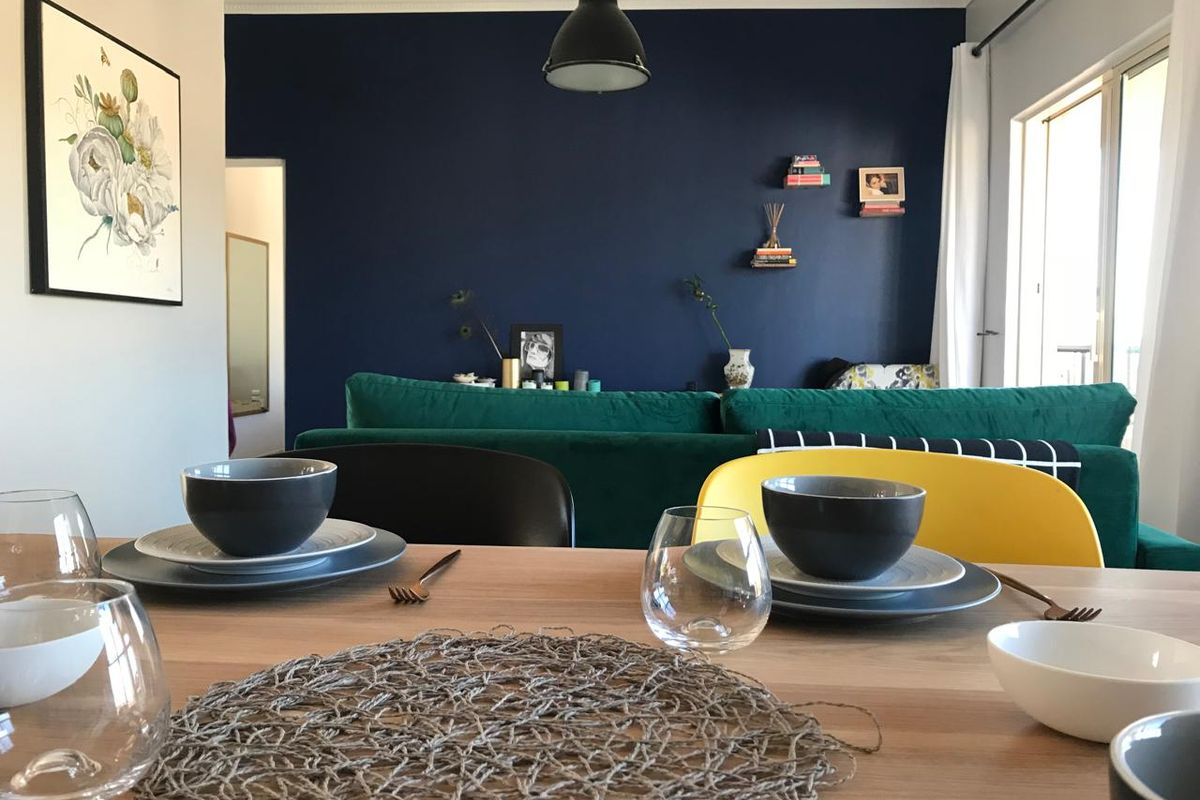 An open-plan living and dining area featuring a bold navy accent wall, modern pendant lighting, and access to an outdoor space via sliding doors.