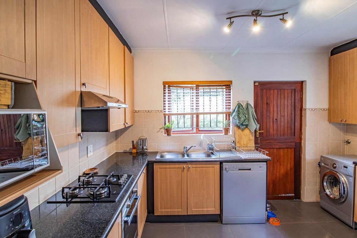 Functional kitchen featuring light wood cabinetry, dark granite countertops, a gas hob, built-in oven, and integrated space for laundry appliances.
