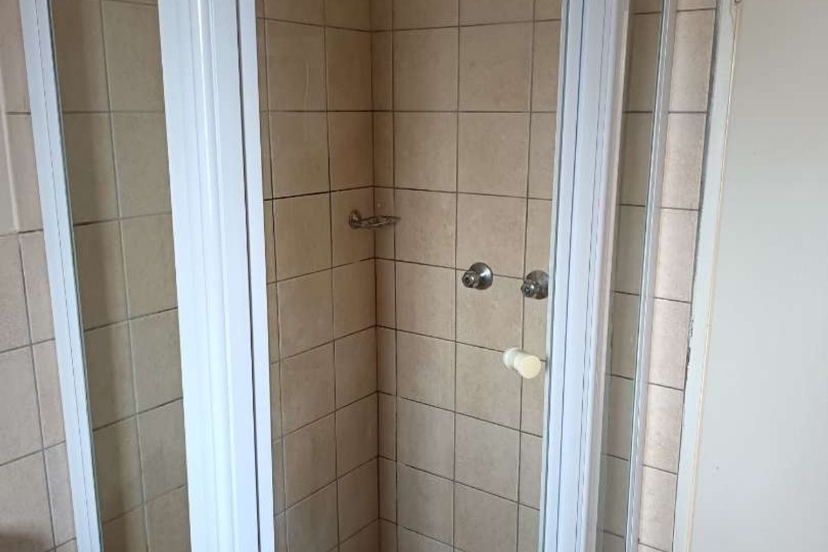 A functional bathroom featuring a corner shower enclosure with tiled walls and flooring, presenting a dated but clean aesthetic.