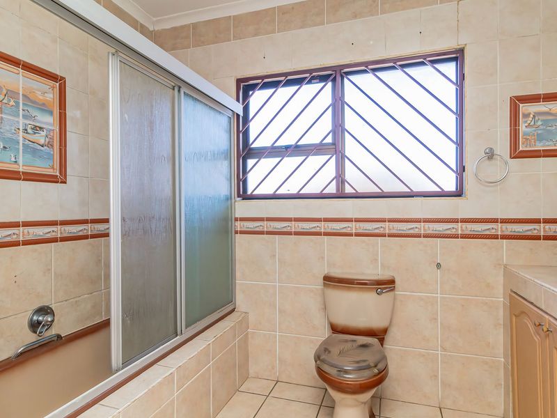 A dated bathroom featuring a built-in bathtub with a sliding screen, a toilet, and a vanity cabinet, finished with neutral wall and floor tiles.